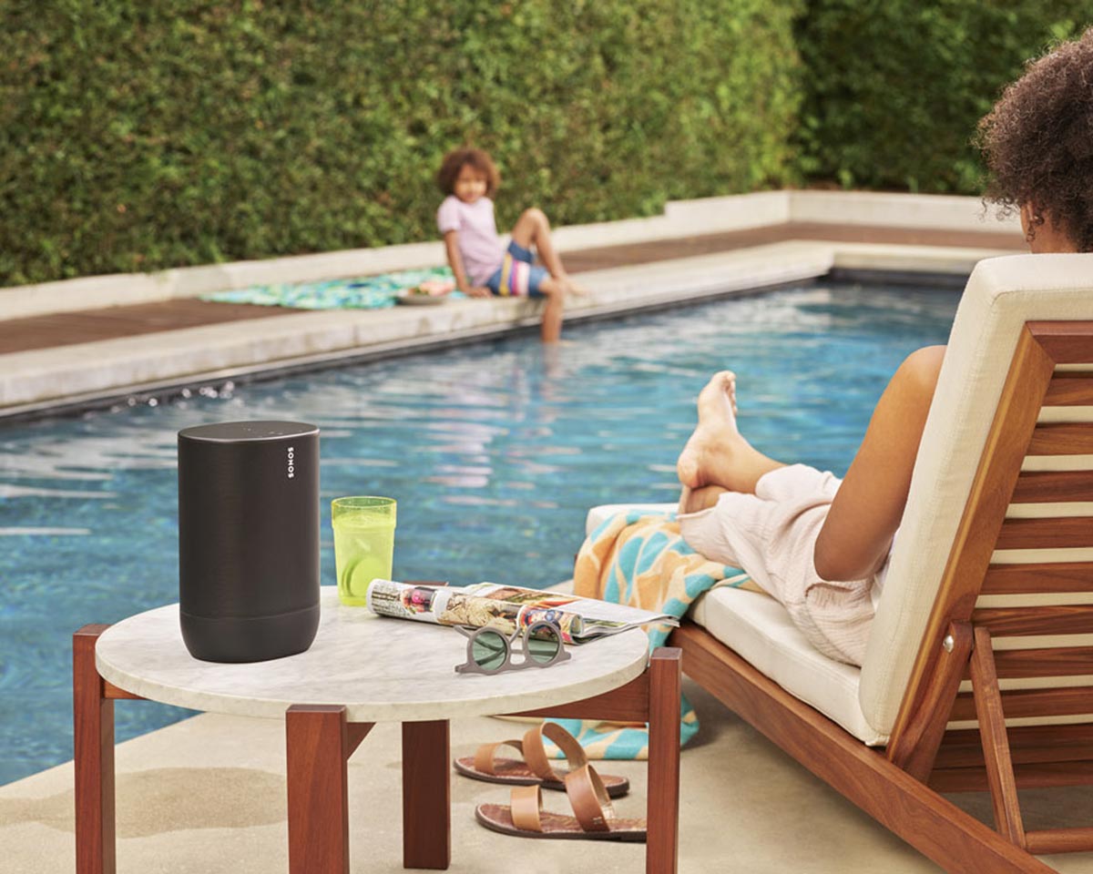person sitting on a chair by the pool with a sonos speaker on a table